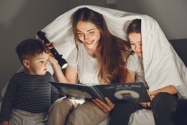 A imagem contém uma mulher seguindo as dicas de bem estar infantil e lendo para suas crianças.