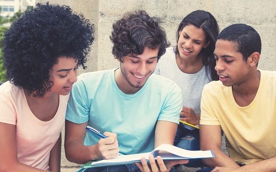 Quatro jovens onde um está ensinando outros três com um caderno e caneta nas mãos