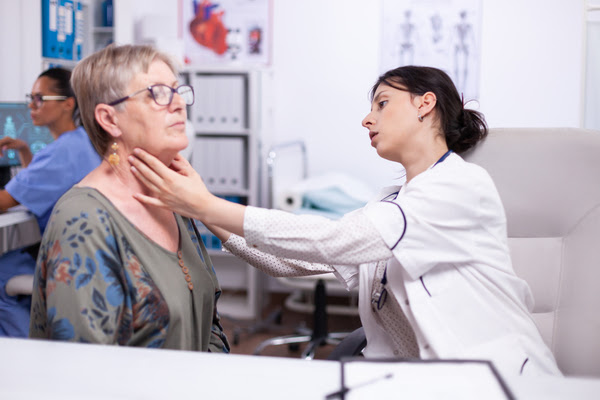 A imagem contém uma médica praticando a Medicina Preventiva na paciente através de exame físico da garganta.