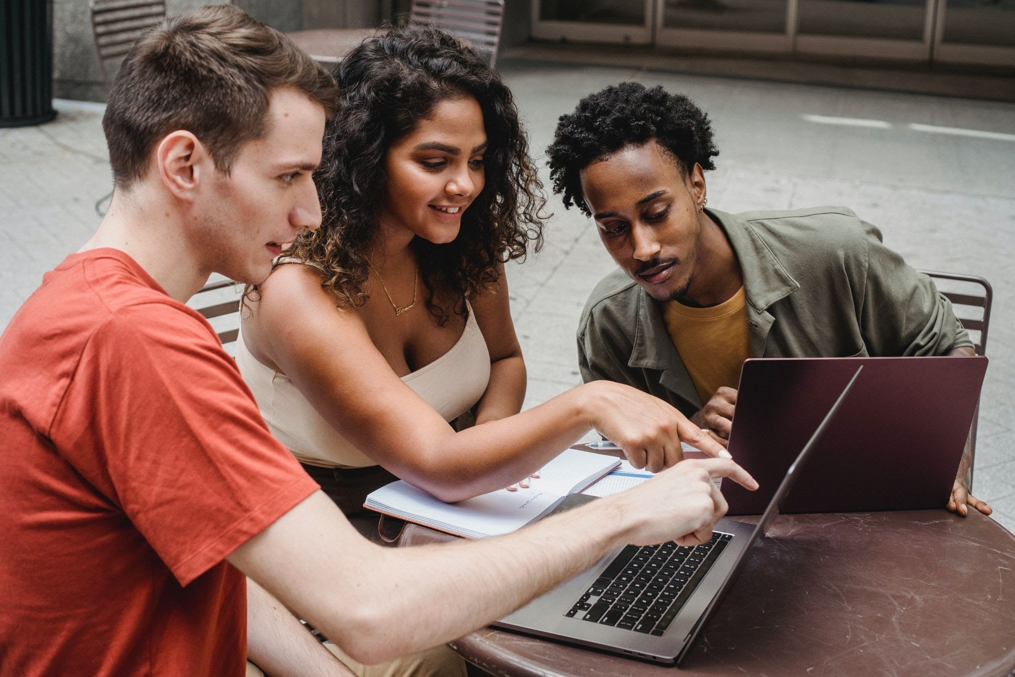 A imagem contém três estudantes, uma jovem e dois jovens, olhando no notebook a notícia sobre o rebranding da Wyden Educacional.